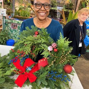 A woman proudly holds a festive Christmas wreath with red and blue decorations.