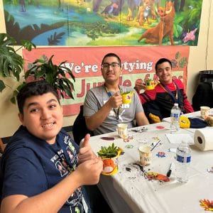 Three boys sitting at a table, enjoying drinks and snacks together.
