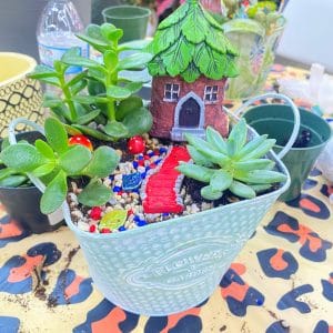 A charming succulent garden in a decorative white pot with a fairy house and tiny figurines.