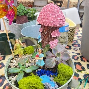 A whimsical fairy garden with miniature figures and a pink mushroom house.