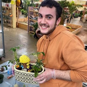A smiling man holding a decorative planter with small plants indoors.