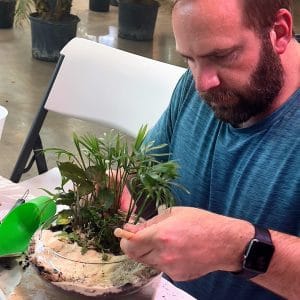 Man carefully tending to a small indoor plant arrangement.