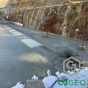 A CJGeo crew pumps CJFill-Ultra Lightweight cellular concrete to backfill an excavation around culvert pipes at the base of a tall, stabilized rock cut.