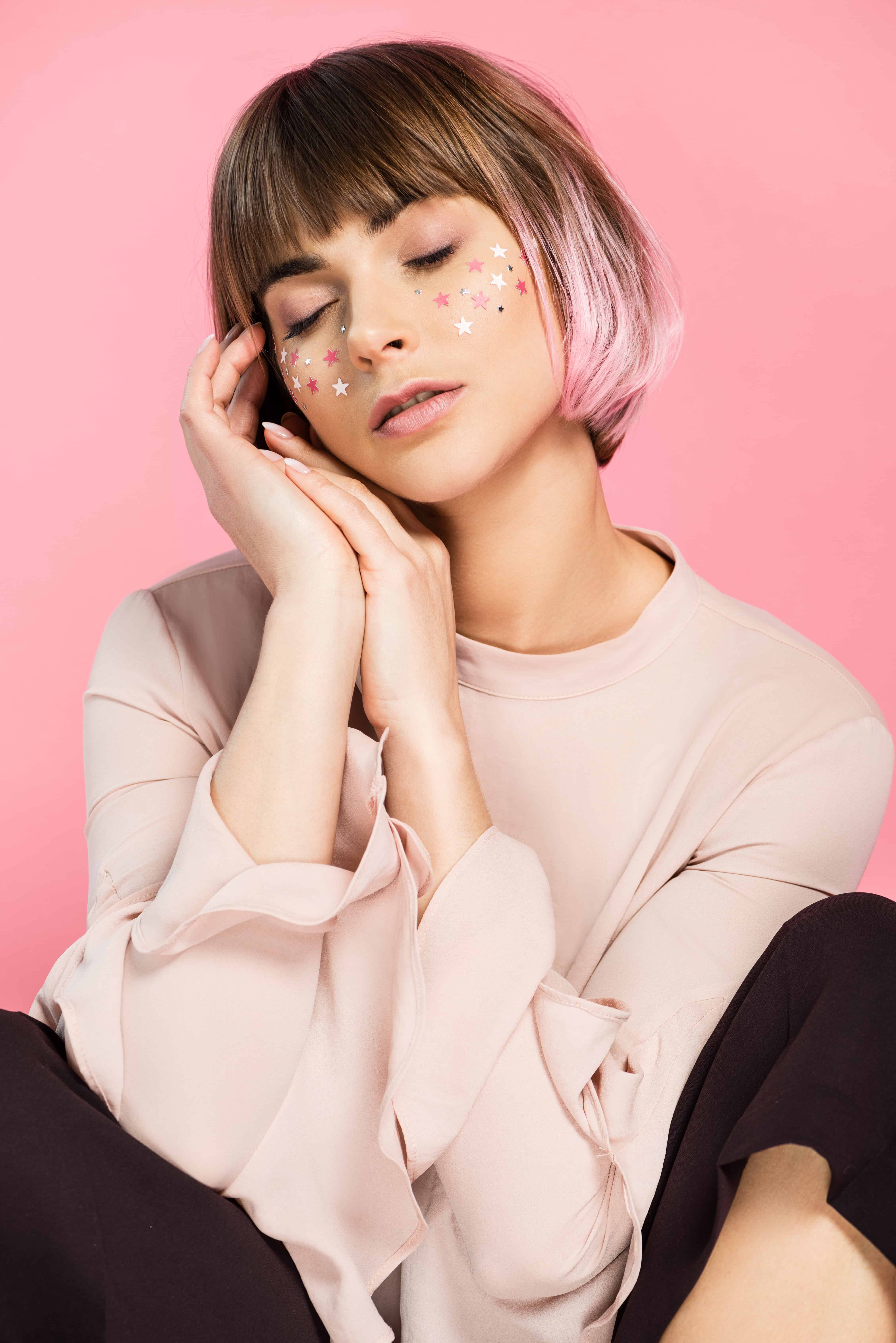 Blonde and pink haired woman with eyes closed and hands resting on face