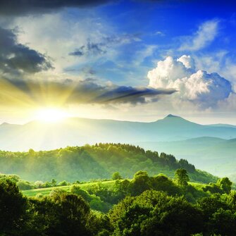 Sunlit green forest landscape with rolling hills, mountain peaks, and dramatic cloudscape — representing the natural environments protected through EDGE Engineering's environmental consulting, permitting, and ecological assessment services.