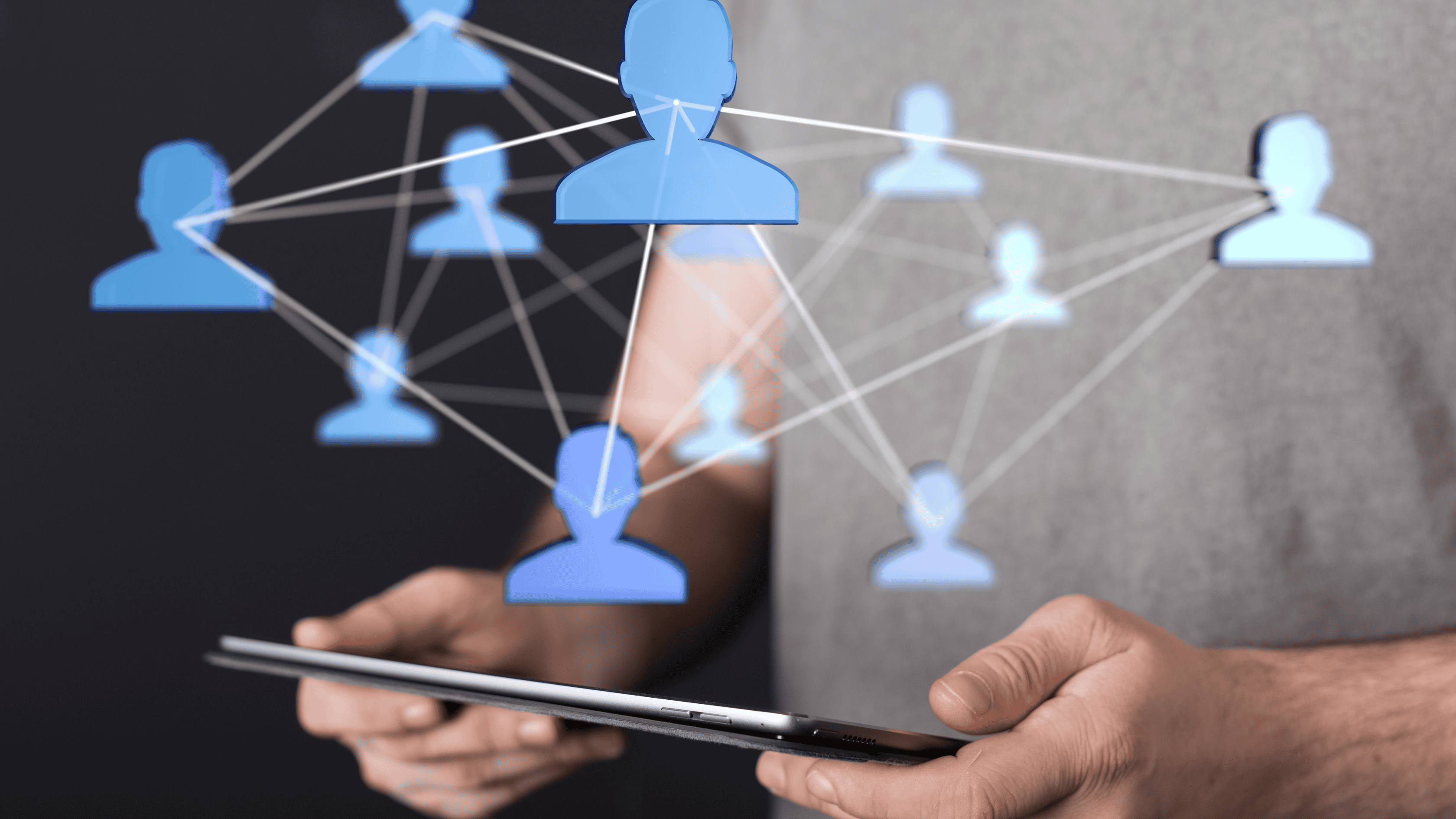 A person holding a tablet with a digital network of blue human icons connected by lines.