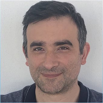 Zdjęcie przedstawia mężczyznę ubranego w ciemny sweter, uśmiechającego się, podczas wydarzenia naukowego związane z ryzykiem i badaniami.