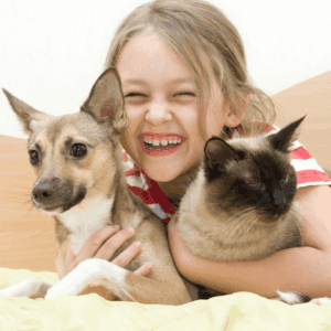 little girl smiles and hugs dog and cat 