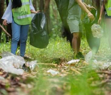 A group of volunteers collecting trash in the forest to save the environment with garbage bags.