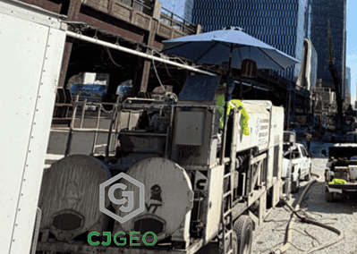 CJGeo cellular concrete batch plant onsite at a construction project with a bridge, fence, and Manhattan skyline in the background.