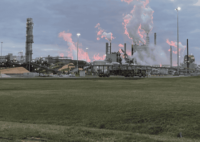 A CJGeo worker pulling a rose through a field with a paper mill in the background during sunset.