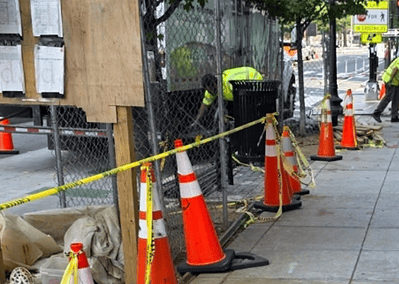 An urban construction site on a sidewalk with cones and a polyurethane grouting truck.