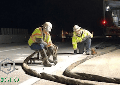 two workers injecting polyurethane grout under concrete pavement at night