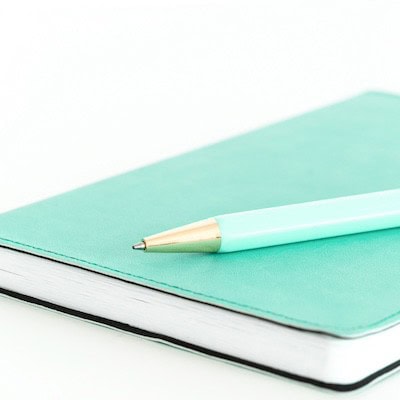 teal notebook and pen against white background on white desktop