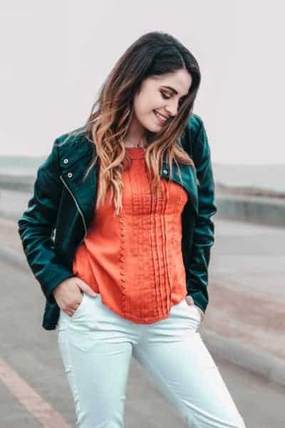 Brunette woman standing on a beach with a smile and hands in her pockets