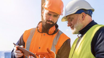 Two men looking at a tablet in safety helmets and gear.