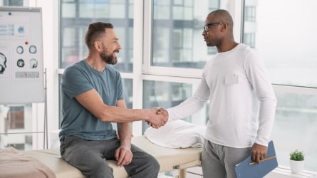 Two men shaking hands in hospital room.
