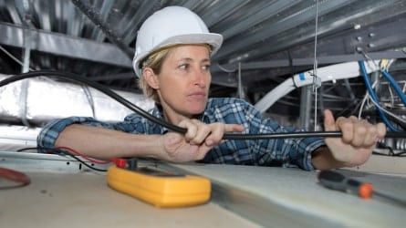 Woman installing electrical wires in small space.