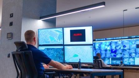 Man sitting in an office monitoring four screens.