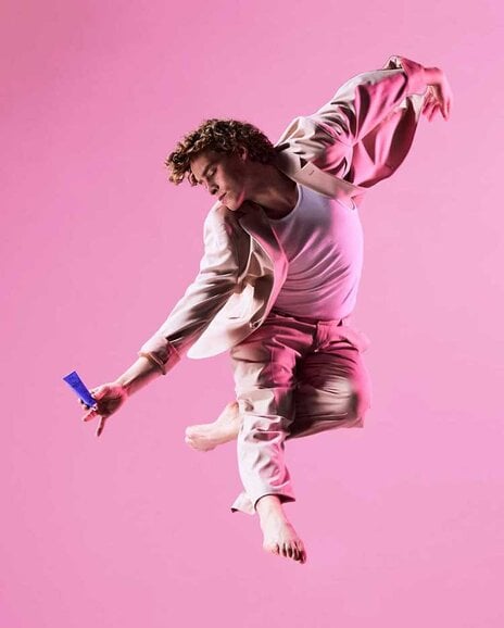 A dancer leaps gracefully, holding tube of deodorant.