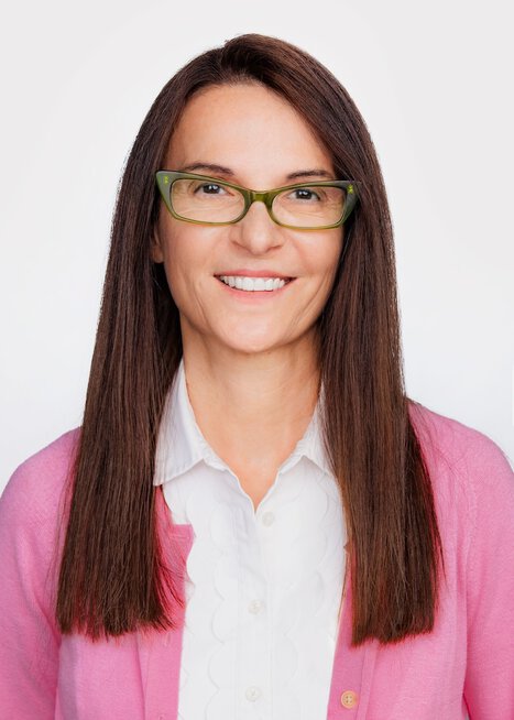 Realtor with brunette long hair, white blouse-pink sweater and green glasses