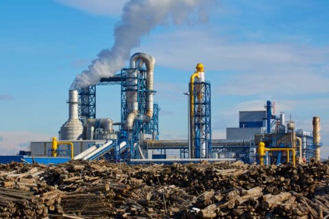 Heavy industrial manufacturing facility with active smokestacks emitting visible emissions surrounded by industrial debris and equipment — major stationary sou…Heavy industrial manufacturing facility with active smokestacks emitting visible emissions surrounded by industrial debris and equipment — major stationary source subject to EPA New Source Review, Title V air permitting, and emissions reduction compliance consulting by EDGE Engineering.