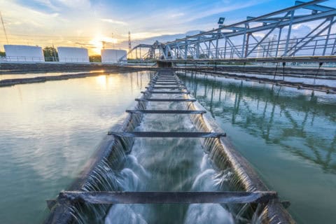 Municipal water treatment facility with flowing water through industrial filtration channels and clarifier tanks at sunset — wastewater treatment infrastructure subject to environmental permitting and regulatory compliance consulting by EDGE Engineering.