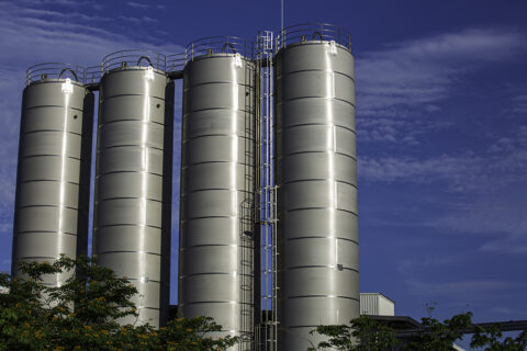 Large stainless steel industrial storage tanks at a chemical or food processing facility against a blue sky — stationary emission sources subject to EPA air permitting, environmental compliance, and regulatory consulting services by EDGE Engineering.