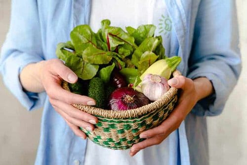 lady holding a basket of veggies.