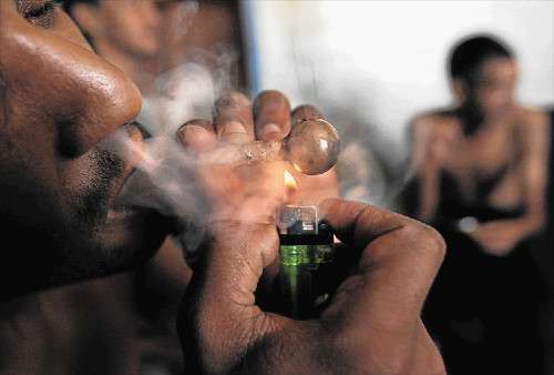 Man smokes tik from gree, glass pipe. Smoke comes from nostrills. In the background in another man. Image : ESA ALEXANDER.