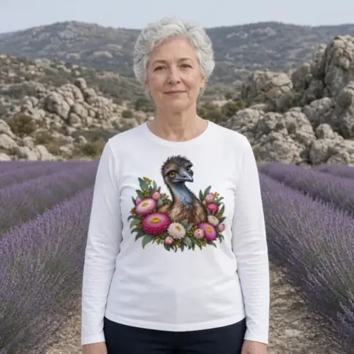 Woman with short grey hair between rows of lavender with granite boulders behind, wearing the white Elegant Emu with Everlasting Daisies women’s long sleeve T-shirt