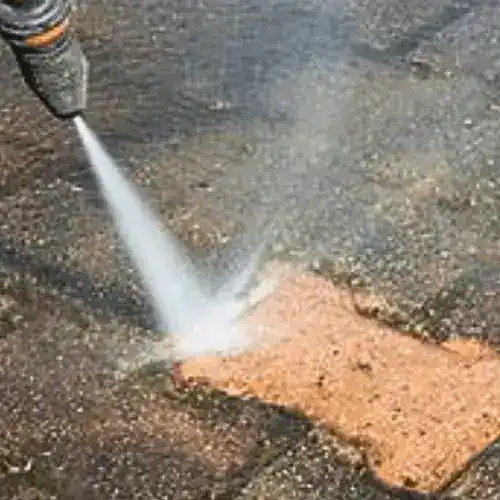 High-pressure water jet cleaning an outdoor driveway surface.