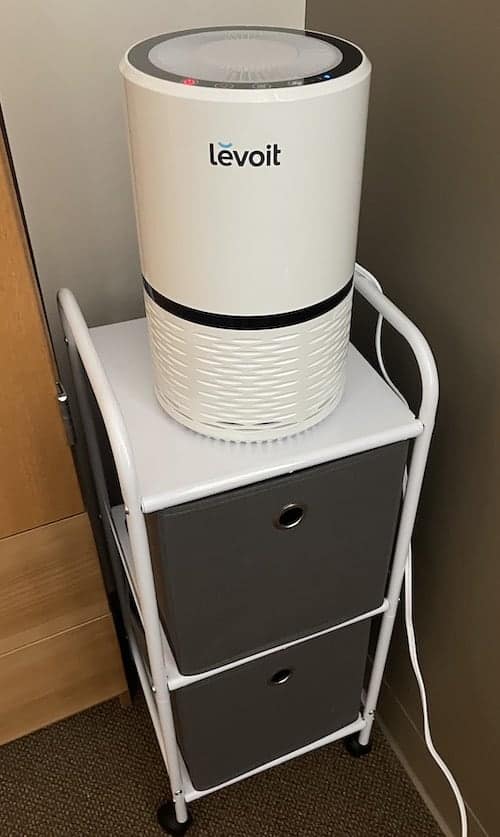 An air purifier sits on top of a rolling cart in a college dorm room