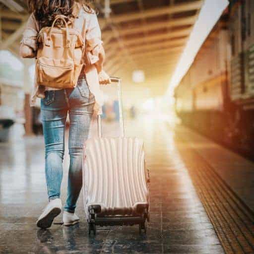 woman rushing to get on a train wearing a backpack and pulling a suitcase