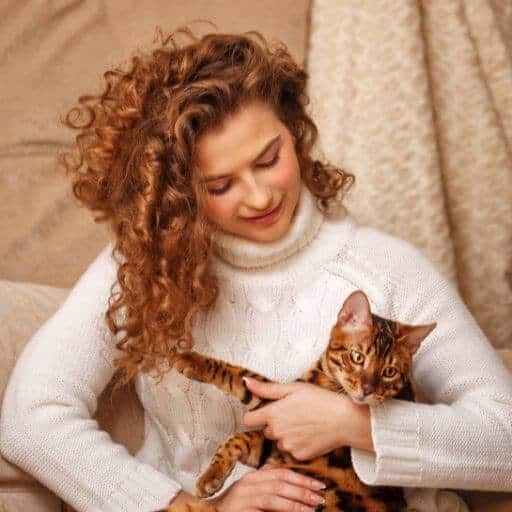 red haired woman wearing a white sweater and holding a bengal cat