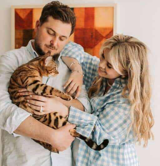 blond woman with a blue plaid shirt and brown haired man in white shirt holding a bengal cat