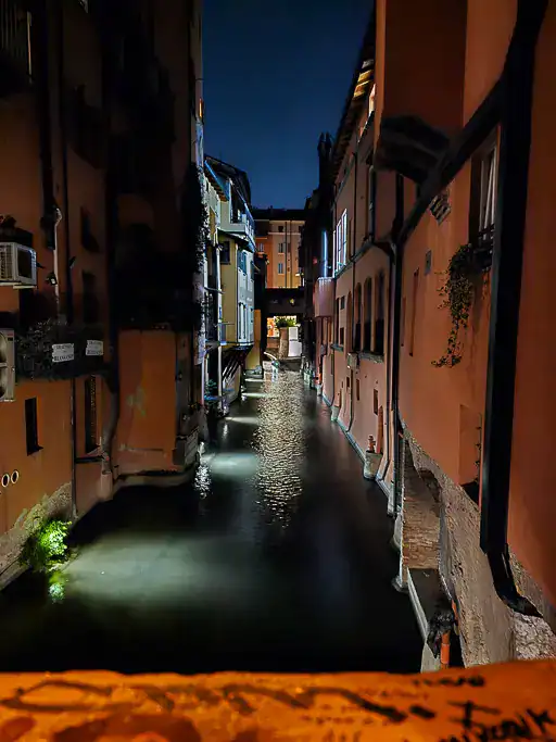 Night view of Bologna’s hidden canal on Via Piella, with softly lit water reflecting historic terracotta-colored buildings — a secret Venetian-style corner in the heart of Bologna that few tourists discover.