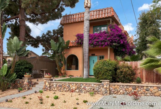 Stunning Spanish-style home at 2416 Vancouver Ave in North Park featuring a terracotta exterior, vibrant purple bougainvillea, a turquoise front door, and a tiered river rock retaining wall.