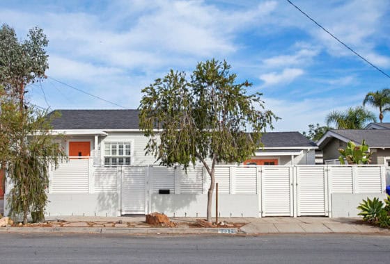 Craftsman-style home at 3382 Redwood Street in North Park featuring a white louvered privacy fence, light grey siding, and vibrant orange front doors.