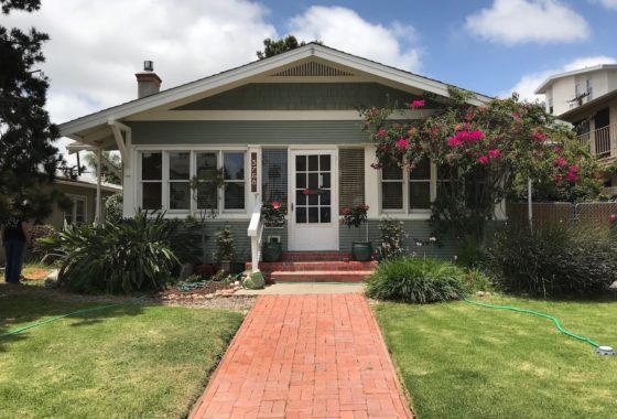 Exterior of a charming green Craftsman bungalow at 3758 31st Street, featuring a red brick walkway, a wide front porch with white trim, and vibrant pink bougainvillea.