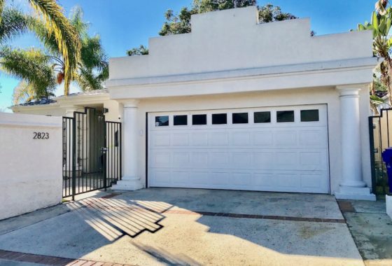 Modern white garage in North Park with Mediterranean-style columns, a stepped parapet roofline, and a gated entryway under bright sunny skies.