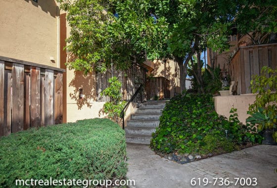 Lushly landscaped walkway at 3761 Villa Terrace in North Park featuring a concrete staircase, mature trees, and verdant hedges leading through a quiet, Mediterranean-style residential complex.