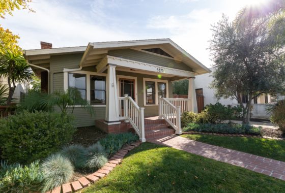Charming Craftsman bungalow in Altadena, in North Park featuring an olive green exterior, white tapered columns on a front porch, and a manicured lawn with a brick pathway.