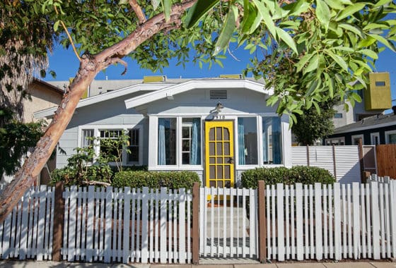 Gated front yard at 2910 Meade in University Heights featuring a white picket fence, landscaped bushes, and a classic brick chimney.