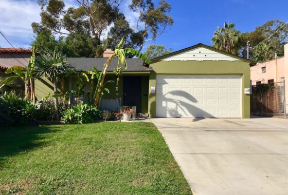 Vibrant olive-green duplex at 1908-10 31st Street in South Park featuring a two-car garage, lush tropical landscaping with banana trees, and a wide concrete driveway under a clear blue sky.