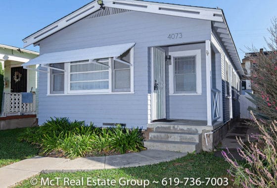 Exterior view of the light blue Craftsman-style home at 4073 34th Street in North Park, featuring a white window awning, a concrete walkway with green landscaping, and a small side-entry porch.