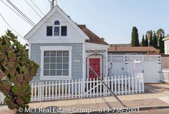 Charming cottage exterior at 1919 Howard Ave in University Heights featuring light grey siding, a bright red front door, decorative white trim, and a classic white picket fence.