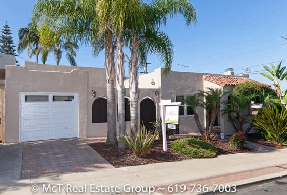 Exterior view of a Spanish-style bungalow featuring a stucco facade, red clay roof tiles, a white garage door, and tropical landscaping with palm trees at 2575 Dwight Street in North Park.