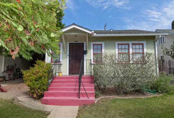 Charming Craftsman-style bungalow exterior at 3811 Alabama Street in North Park, featuring sage green siding, red-trimmed windows, and a vibrant pink front staircase.