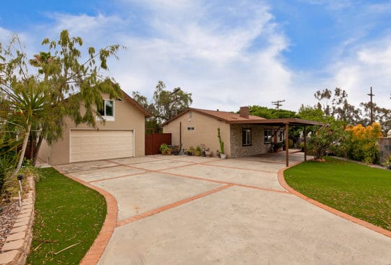 Wide-angle view of the backyard at 3505 Wilson Ave in Cherokee Point, showcasing an expansive concrete driveway with brick borders, a lush green lawn, and the detached two-story garage next to the main residence.